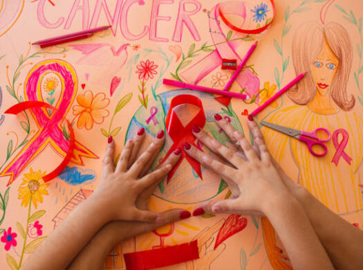 Hands resting on a hand-drawn cancer awareness poster with pink ribbons